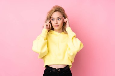 Pembe arka planda izole edilmiş sweatshirt giyen genç sarışın kadının şüpheleri ve düşünceleri var.