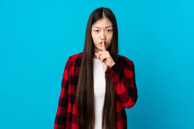 İzole edilmiş mavi arka planda genç bir Çinli kız sessizce hareket ettiğini gösteriyor. Parmağını ağzına sokuyor.