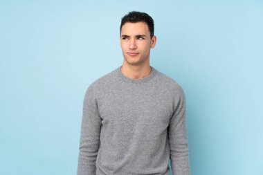 Beyaz tenli yakışıklı adam mavi arka planda izole edilmiş duruyor ve yan tarafa bakıyor.