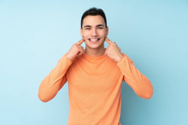 Beyaz tenli yakışıklı adam mavi arka planda izole edilmiş mutlu ve hoş bir ifadeyle gülümsüyor.