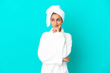 İzole edilmiş mavi arka planda bornozlu genç bir kadının şüpheleri ve düşünceleri var.