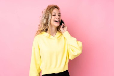 Pembe arka planda eşofman giyen genç sarışın kadın cep telefonuyla sohbet ediyor.