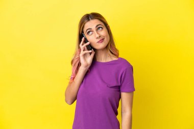 İzole edilmiş sarı arka planda cep telefonu kullanan genç bir kadın.
