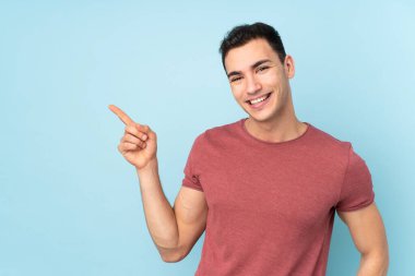 Beyaz tenli yakışıklı adam mavi arka planda izole edilmiş, parmağıyla kenarı gösteriyor.