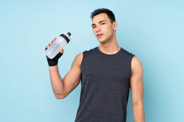 Genç sporcu, mavi arka planda izole edilmiş, su şişesiyle geziyor.