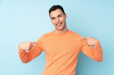 Mavi arka planda soyutlanmış, gururlu ve kendini beğenmiş beyaz, yakışıklı genç bir adam.