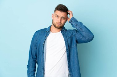 Rus yakışıklı adam mavi arka planda izole edilmiş, hayal kırıklığı ifadesi var ve anlamıyor.