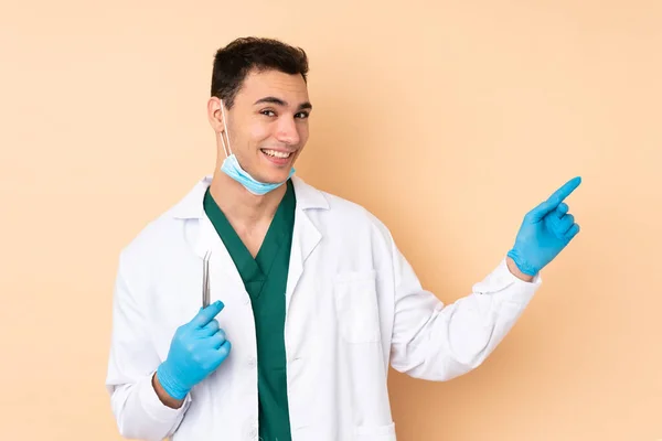 Young Dentist Man Holding Tools Isolated Beige Background Pointing Finger — Stock Photo, Image