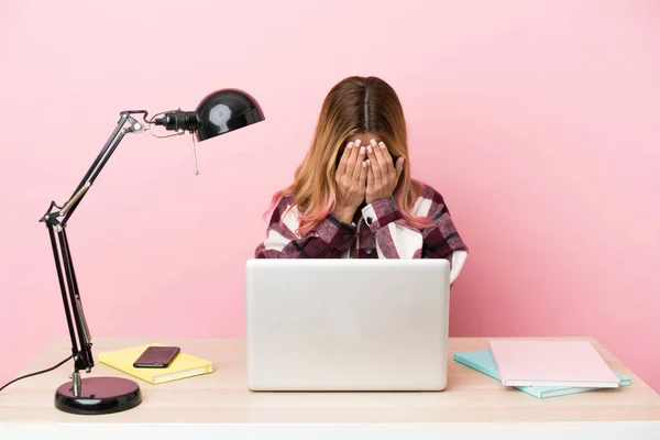 Young student woman in a workplace with a laptop over pink background with tired and sick expression