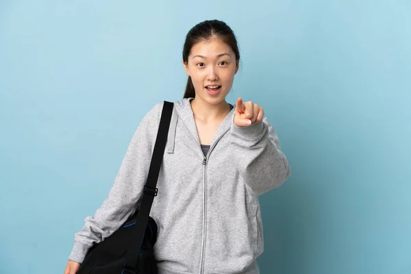 年轻的中国女子 背着运动包 蓝色背景 惊讶地指着前方 — 图库照片