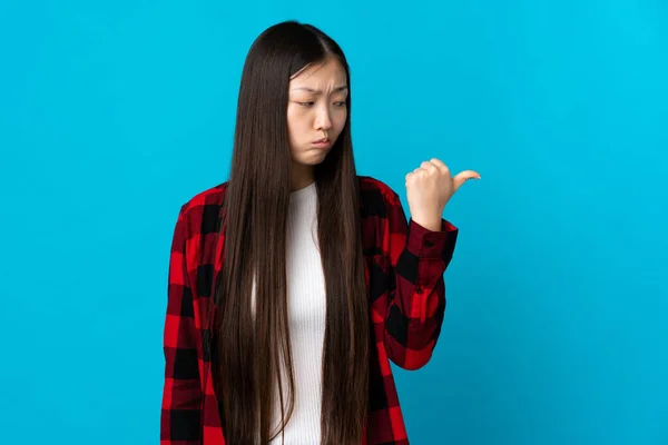 Młoda Chińska Dziewczyna Odizolowanym Tle Niebieski Nieszczęśliwy Wskazując Bok — Zdjęcie stockowe