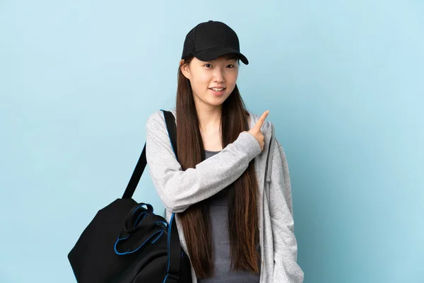 年轻的中国女子体育运动员 背着运动包 蓝色的孤立的背景 惊讶而又有针对性的侧面 — 图库照片