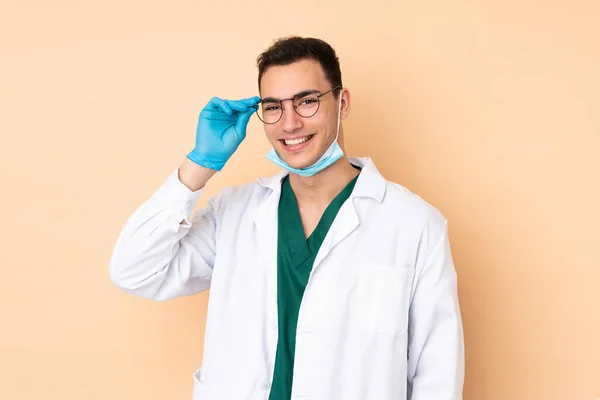 Νεαρός Οδοντίατρος Κρατώντας Εργαλεία Απομονώνονται Μπεζ Φόντο Γυαλιά Και Έκπληκτος — Φωτογραφία Αρχείου