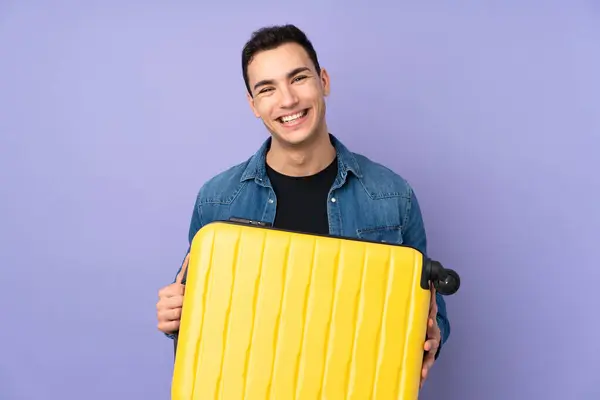 若いですCaucasianハンサムな男隔離上の紫の背景で休暇で旅行スーツケース — ストック写真