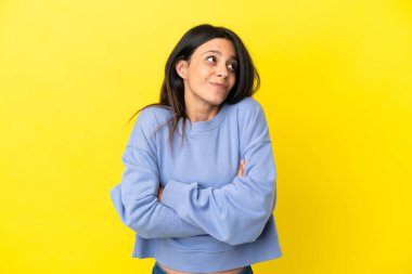 Sarı arka planda izole edilmiş genç, beyaz bir kadın omuzlarını kaldırırken şüpheyle hareket ediyor.