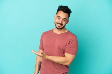 Mavi arka planda izole edilmiş genç beyaz adam gülümserken bir fikir sunuyor.