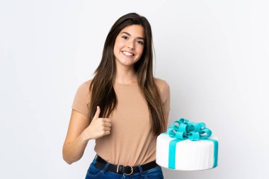 Ergen pasta şefi izole edilmiş beyaz arka planda büyük bir pasta tutuyor. Başparmakları havada çünkü iyi bir şey oldu.