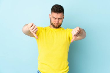 Mavi arka planda izole edilmiş, iki eliyle baş parmağını gösteren Rus yakışıklı bir adam.