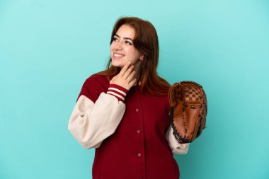 Beyzbol oynayan genç kızıl saçlı kadın mavi arka planda izole edilmiş gülümserken yukarı bakıyor.