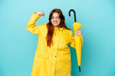 Mavi arka planda şemsiyesi olan kızıl saçlı kadın güçlü bir jest yapıyor.