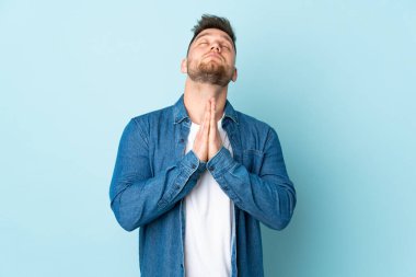 Mavi arka planda izole edilmiş Rus yakışıklı adam avuç içlerini bir arada tutuyor. İnsan bir şey ister.