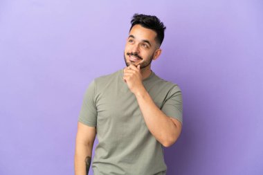 Mor arka planda izole edilmiş genç beyaz adam gülümserken yukarı bakıyor.