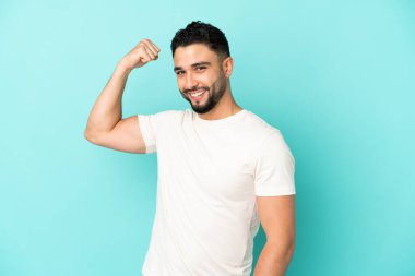 Genç Arap adam mavi arka planda izole edilmiş güçlü bir jest yapıyor.