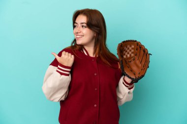 Beyzbol oynayan genç kızıl saçlı kadın, mavi arka planda soyutlanmış bir şekilde bir ürünü sunmak için kenarı işaret ediyor.