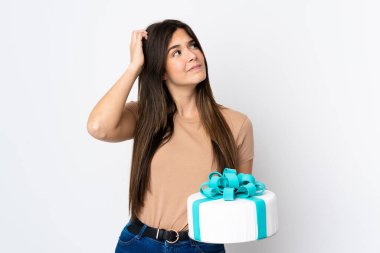 Genç pasta şefi, izole edilmiş beyaz arka plan üzerinde büyük bir pasta tutuyor. Şüpheleri var ve kafası karışmış bir yüz ifadesi var.