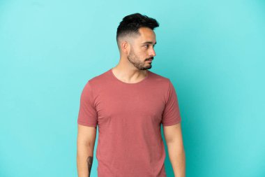 Mavi arka planda izole edilmiş genç beyaz adam yan tarafa bakıyor.