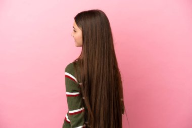 Küçük kız pembe arka planda izole edilmiş ve arkasına bakıyor.