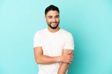 Genç Arap adam mavi arka planda yalnız gülüyor.