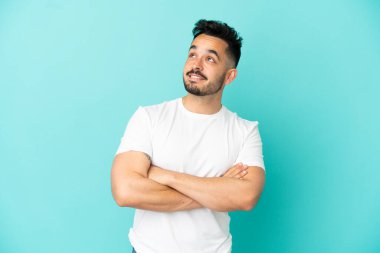 Genç beyaz adam mavi arka planda izole edilmiş gülümserken yukarı bakıyor.