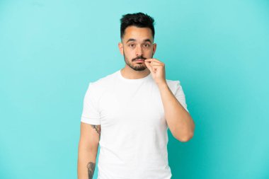 Mavi arka planda izole edilmiş genç beyaz bir adam sessizlik işareti gösteriyor.