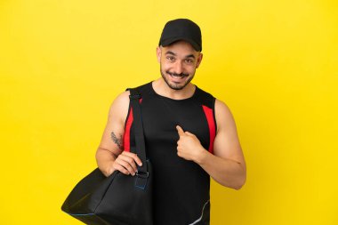 Spor çantalı genç beyaz adam, sarı arka planda, şaşırmış bir yüz ifadesiyle izole edilmiş.
