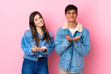 İzole edilmiş pembe arka planı olan genç bir çift, fotokopi alanı hayali bir ilan vermek için avuçlarında tutuyorlar.