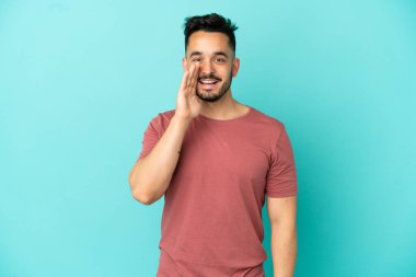 Mavi arka planda izole edilmiş genç beyaz adam ağzı açık bağırıyor.