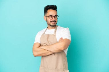 Restoran garsonu beyaz adam mavi arka planda izole edilmiş, kolları bağlı ve mutlu.