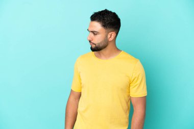 Genç Arap adam mavi arka planda izole edilmiş, yana bakıyor.