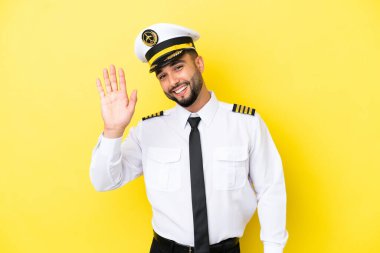 Arap uçak pilotu, sarı arka planda izole edilmiş mutlu bir ifadeyle selamlıyor.
