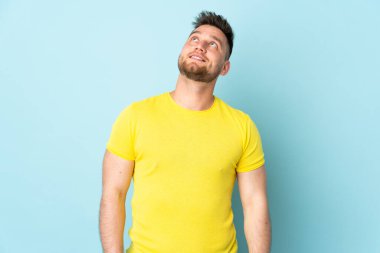 Rus yakışıklı adam mavi arka planda izole edilmiş bir şekilde yukarı bakarken bir fikir düşünüyor.