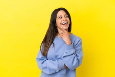 Sarı arka planda izole edilmiş genç beyaz kadın gülümserken yukarı bakıyor.