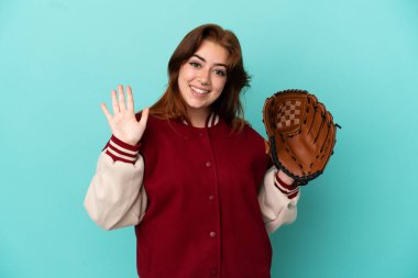Beyzbol oynayan genç kızıl saçlı kadın mavi arka planda soyutlanmış, mutlu bir ifadeyle selamlıyor.