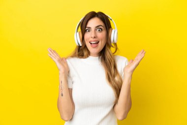 Sarı arka planda izole edilmiş beyaz kadın şaşırdı ve müzik dinliyor.