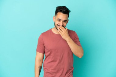 Mavi arka planda izole edilmiş genç beyaz adam mutlu ve gülümsüyor.