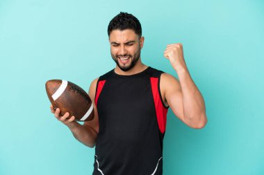 Genç Arap rugby oynayan adam mavi arka planda izole edilmiş zaferi kutluyor.