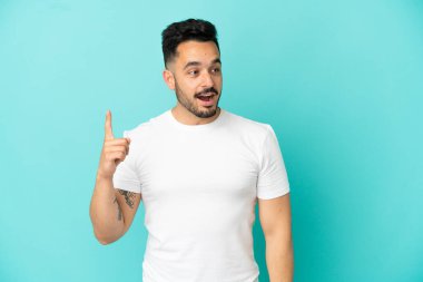 Kafkasyalı genç adam mavi arka planda izole edilmiş bir şekilde parmağını kaldırarak çözümü anlamaya çalışıyor.