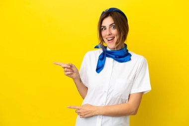 Sarı arka planda izole edilmiş uçak hostesi kadın şaşırmış ve işaret ediyor.