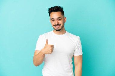 Kafkasyalı genç adam mavi arka planda izole edilmiş bir şekilde baş parmak işareti yapıyor.