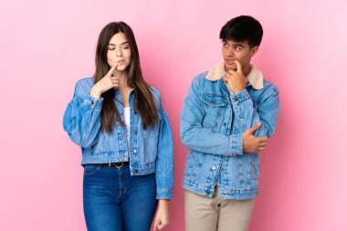 Soyutlanmış pembe arka planı olan genç bir çift yukarı bakarken şüphe duyuyor.